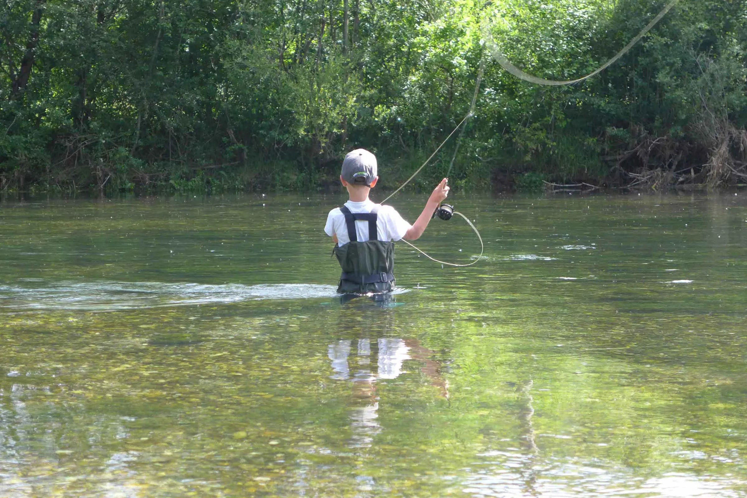 Small child fly fishing up to their waist in river