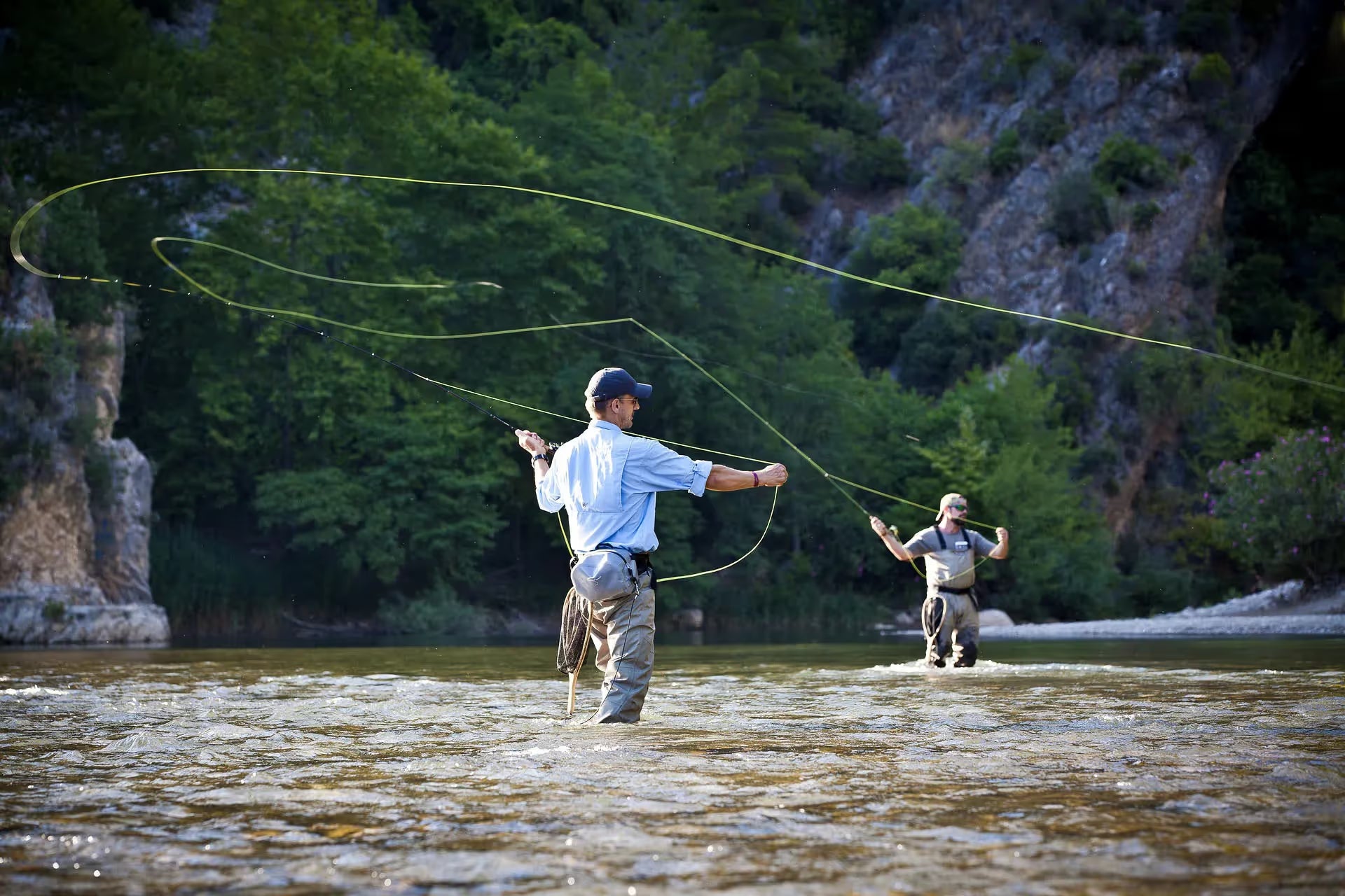 Two anglers stood in a river up the their knees fly fishing.
